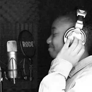 Black and white photograph of youth wearing headphones recording rap vocals at APMF Hip Hop Institute studio with professional microphone.