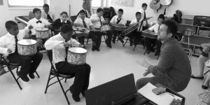 Black and white photo overhead view of music students in uniform playing drums during class instruction.