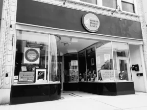 Black and white photograph of Asbury Park 'Where Music Lives' storefront entrance with circular signage and large display windows.